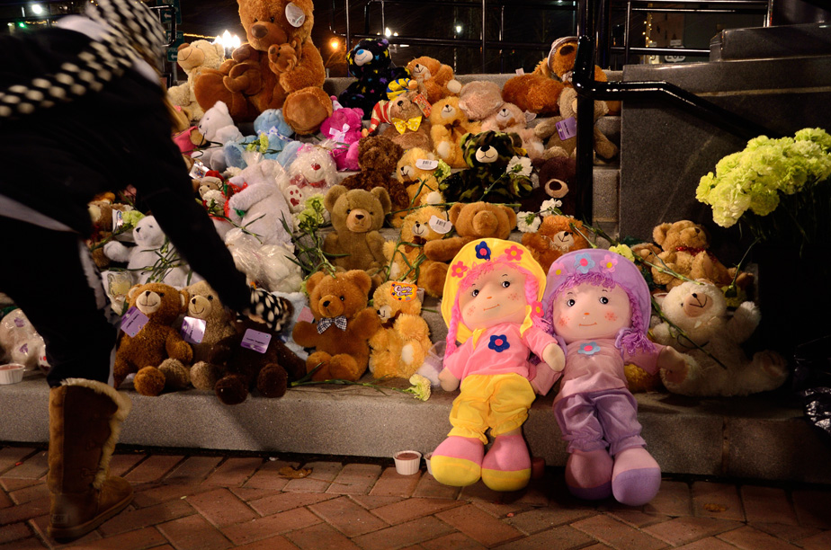 A young woman places a stuffed bear at a memorial.