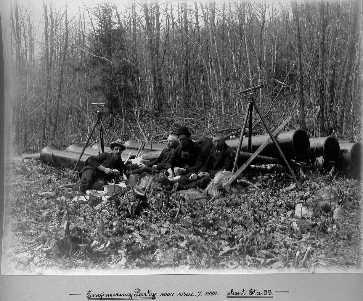 Engineering men sitting on ground eating their lunch next to water pipes